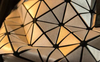 Close-up of a geometric, triangular-patterned metallic surface with reflective silver and gold tones, resembling a modern tessellated design on a fashion accessory or architectural element