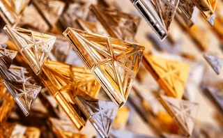 Abstract composition of floating, transparent triangular forms in gold, bronze and silver tones, creating a layered geometric pattern against a softly blurred background