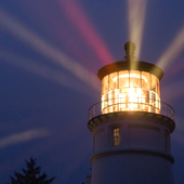 A lighthouse beaming rays of light into dark evening sky