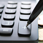 Calculator next to a pile of coins with a pen poised to press the plus key